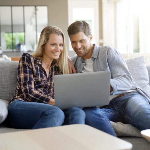 Cheerful couple at home using laptop